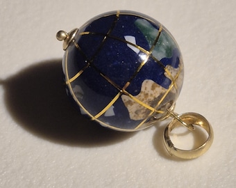 May include: A gold globe pendant with a blue lapis lazuli stone and gold accents. The globe is a detailed representation of the Earth with continents and oceans.
