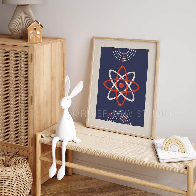 Puede incluir: Una impresi&oacute;n art&iacute;stica enmarcada con un fondo azul marino presenta un dise&ntilde;o de &aacute;tomo blanco y rojo. Una figura de conejo blanco se sienta en un banco tejido junto a la obra de arte enmarcada. Una peque&ntilde;a casa de madera y una l&aacute;mpara est&aacute;n en un mueble de madera.