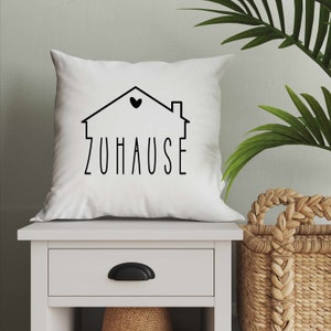 May include: White throw pillow with a black outline of a house with a heart in the window and the word "ZUHAUSE" underneath.