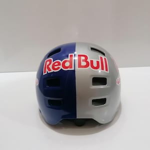 May include: A Red Bull branded helmet, split vertically with a blue and silver color scheme. The Red Bull logo is prominently displayed in red and white. The helmet has multiple ventilation slots.