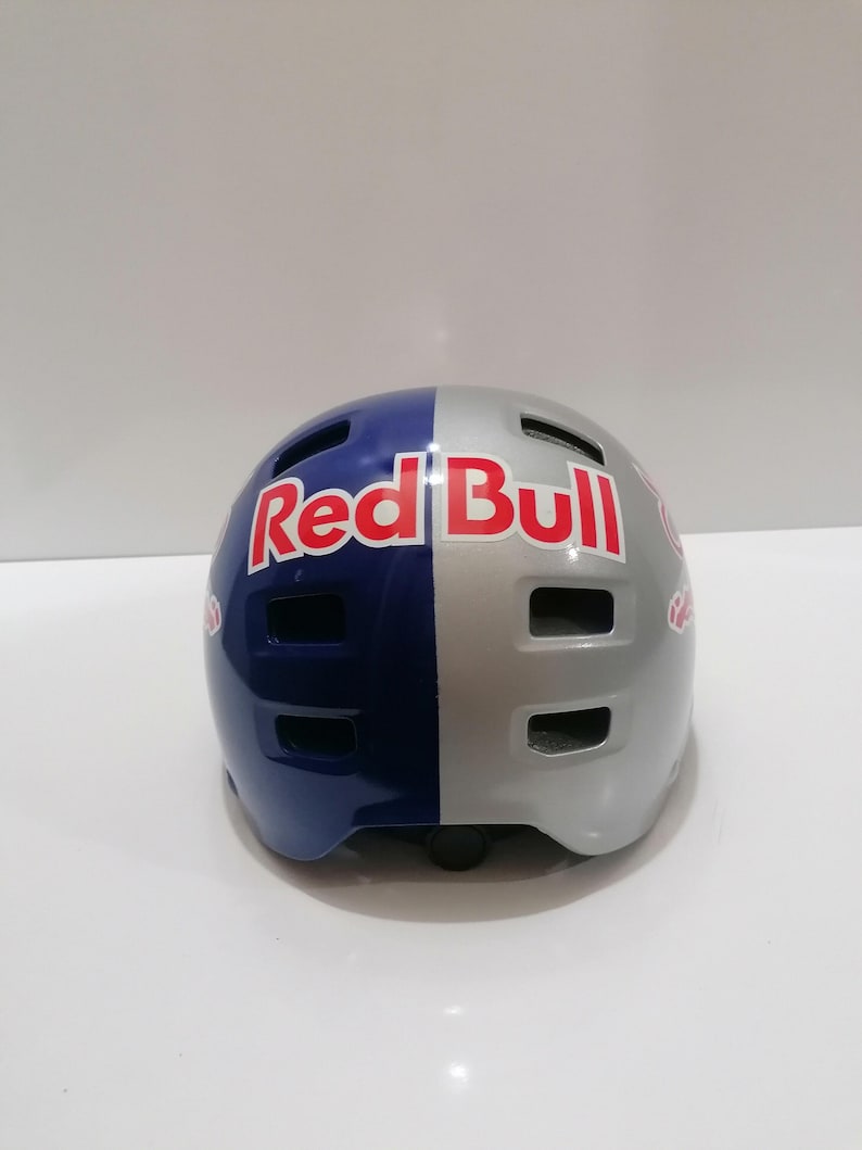 May include: A Red Bull branded helmet, split vertically with a blue and silver color scheme. The Red Bull logo is prominently displayed in red and white. The helmet has multiple ventilation slots.