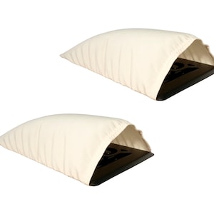 May include: Two cream-colored, pillow-shaped cases, each with a black rectangular object partially visible inside. The cases have a soft, pleated texture and a rounded shape, suggesting they are designed for protection.