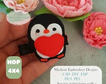 May include: A black, white, and red penguin-shaped applique holding a red heart. The applique is surrounded by pink felt flowers. The image includes text that reads "Machine Embroidery Designs" and "HOP 4X4".