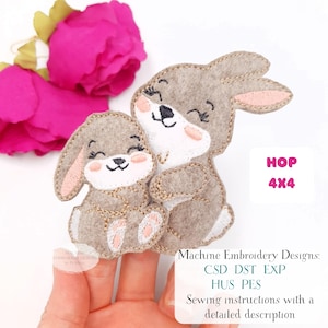 May include: A felt applique featuring two smiling bunnies, one embracing the other. The bunnies are light brown with pink accents and stitched details. The text "HOP 4x4" is visible. The design is for machine embroidery.
