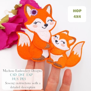 May include: Two orange felt fox appliqués, one larger and one smaller, are shown. The larger fox has a purple flower on its head. The smaller fox is nestled against the larger one. The text "HOP 4X4" is in the upper right corner. The text "Machine Embroidery Designs" and other text are in the lower left corner.