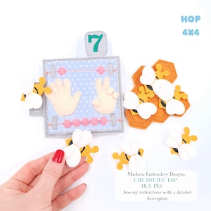 May include: A felt educational toy with a blue polka-dot background, featuring the number 7, hand shapes, and bee-themed elements. The text "HOP 4x4" is visible. Includes machine embroidery designs and sewing instructions.