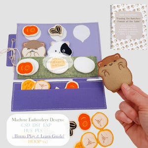 May include: A felt play set with a purple background, featuring embroidered food items and hamster figures. The set includes a booklet with instructions. The text on the set reads "Machine Embroidery Designs" and "Feeding the Hamsters: Friends at the Table".
