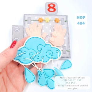 May include: A felt educational toy featuring a cloud with raindrops, a number 8, and hand shapes. The toy is in shades of grey, light blue, and peach. The text "HOP 4x4" is visible. Designed for learning and play, it's a tactile learning tool.