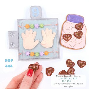 May include: A felt activity book with a light blue background, featuring hand shapes, colourful beads, and a jar with heart-shaped appliques. The book has a grey border and a button closure. The text "HOP 4X4" is visible.