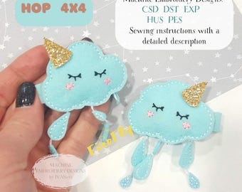 May include: Two light blue cloud-shaped hair clips with closed eyes, pink cheeks, and gold glitter horns. Each clip has dangling rain drops. The image also includes text that says "HOP 4X4" and "Machine Embroidery Designs".