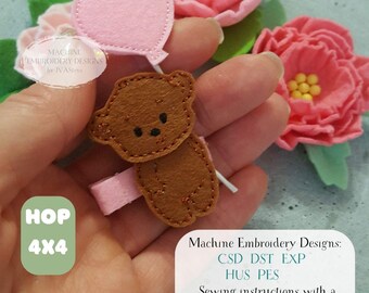 May include: A brown felt teddy bear holding a pink heart-shaped balloon, with a pink hair clip. The image includes text that reads "Machine Embroidery Designs" and "HOP 4x4". Pink felt flowers are in the background.