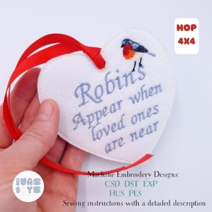 May include: A white heart-shaped embroidered ornament with a red ribbon. The ornament features a blue embroidered message that reads "Robin's Appear when loved ones are near" and a small bird illustration. The text "HOP 4x4" is in the upper right corner.