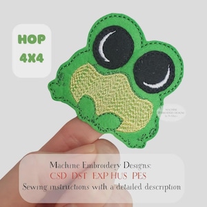 May include: A green frog-shaped embroidery design with large black eyes and a textured, light-yellow mouth. The design includes the text "HOP 4x4" and "Machine Embroidery Designs".