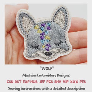 May include: A grey felt wolf head patch with embroidered details in purple, yellow, and blue. The patch has a white border and is labelled "WOLF". The image also includes text about machine embroidery designs and sewing instructions.
