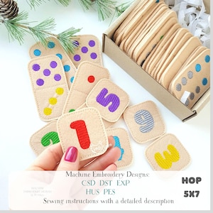 May include: A collection of beige felt dominoes and number tiles with colourful embroidered details. The dominoes feature dots, while the tiles display numbers 1-9 in various colours. The image includes text: Machine Embroidery Designs, CSD DST EXP, HUS PES, HOP 5X7.