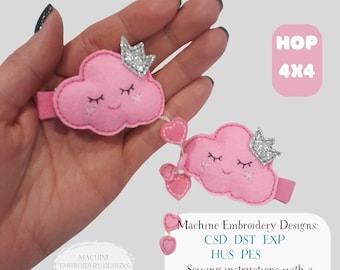 May include: Two pink cloud-shaped hair clips with silver glitter crowns and embroidered faces. The clips are connected by pink heart-shaped charms. The image includes text that says "HOP 4x4" and "Machine Embroidery Designs" with sewing instructions.