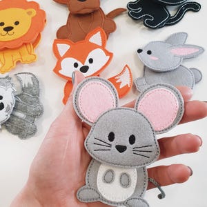 May include: A collection of colorful felt animal figures, including a gray mouse with pink ears, a brown dog, an orange fox, a black cat, a gray rabbit, and a yellow lion. Each figure is hand-stitched with contrasting thread.