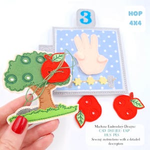 May include: A felt educational toy with a tree and a red apple, a hand showing three fingers, and the number 3. The toy has a blue polka-dot background and additional red apple cutouts. The text "HOP 4x4" is visible.