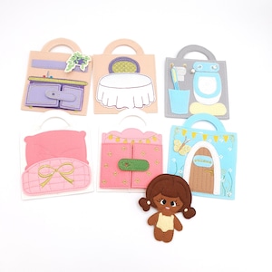 May include: A collection of felt activity bags, each depicting a different room or object, including a bathroom, bedroom, and kitchen. A felt doll is also included. The bags are in various colors, with details like a table, toilet, and bed.