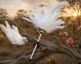 May include: A cat toy wand featuring a cluster of long white feathers attached to a handle. The handle is decorated with a band of small clear crystals, a series of white spherical beads, and a textured silver-toned shaft with black accents.