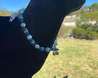 May include: A beaded bracelet featuring blue and white beads, interspersed with silver-toned accents. The bracelet has a silver charm shaped like a bee and a silver charm shaped like a butterfly.