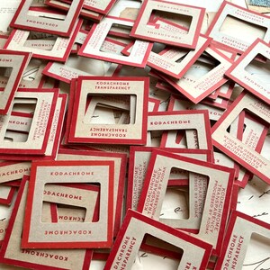 May include: A collection of square cardboard slide mounts with red borders and tan centers. Each mount features the text KODACHROME TRANSPARENCY PROCESSED BY KODAK printed in red ink. The slides are scattered in an overlapping arrangement.