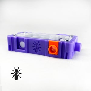 May include: A purple ant farm with a clear plastic viewing area and an orange ventilation port. The ant farm has a black ant logo on the side.