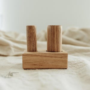 May include: A wooden desk organizer with two cylindrical holders and a rectangular base. The wood has a natural grain pattern and a light brown color. The organizer is designed to hold pens, pencils, or other small office supplies.