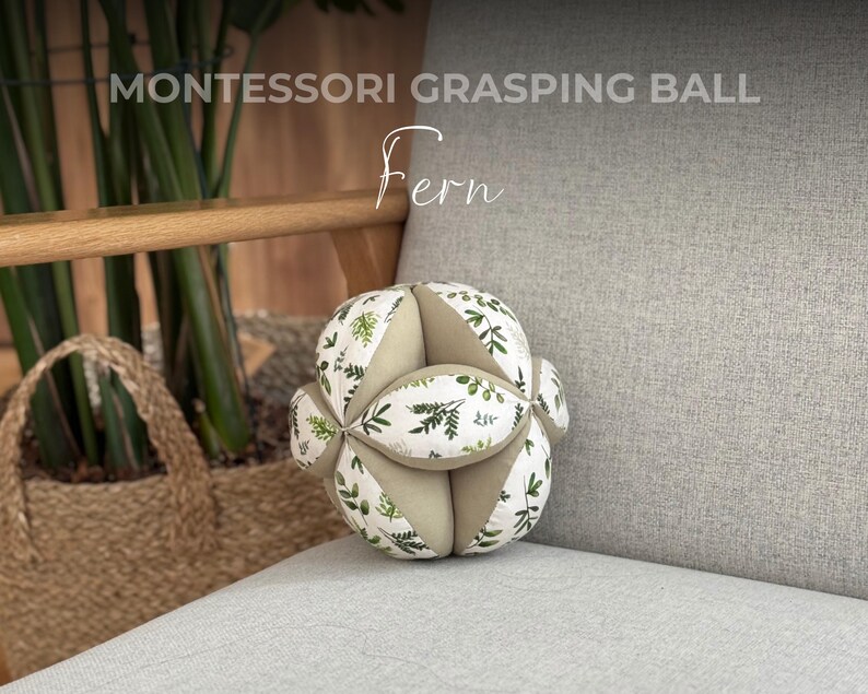 May include: A Montessori grasping ball with a white background and green leaf pattern. The ball is labeled "Fern".