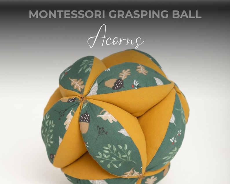 May include: A yellow and green fabric ball with an acorn and leaf pattern. The ball is made of soft fabric and is designed for grasping and sensory play. Montessori Grasping Ball Acorns.