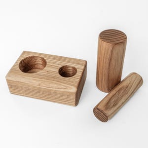 May include: A wooden desk organizer with two circular cutouts, a tall cylinder, and a shorter, rounded piece. The items are made of light brown wood with visible grain and are arranged on a white surface.