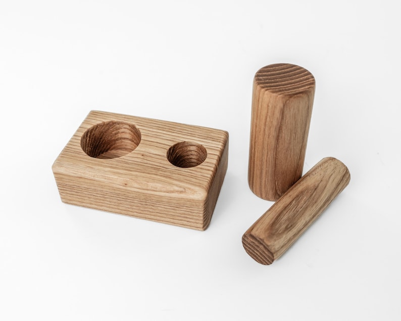 May include: A wooden desk organizer with two circular cutouts, a tall cylinder, and a shorter, rounded piece. The items are made of light brown wood with visible grain and are arranged on a white surface.