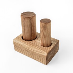 May include: A wooden desk organizer with two cylindrical holders. The organizer is made of light brown wood and has a rectangular base. The cylindrical holders are of different heights and are designed to hold pens or pencils.