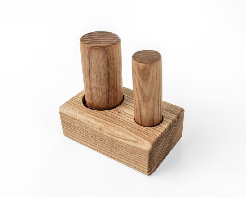 May include: A wooden desk organizer with two cylindrical holders. The organizer is made of light brown wood and has a rectangular base. The cylindrical holders are of different heights and are designed to hold pens or pencils.