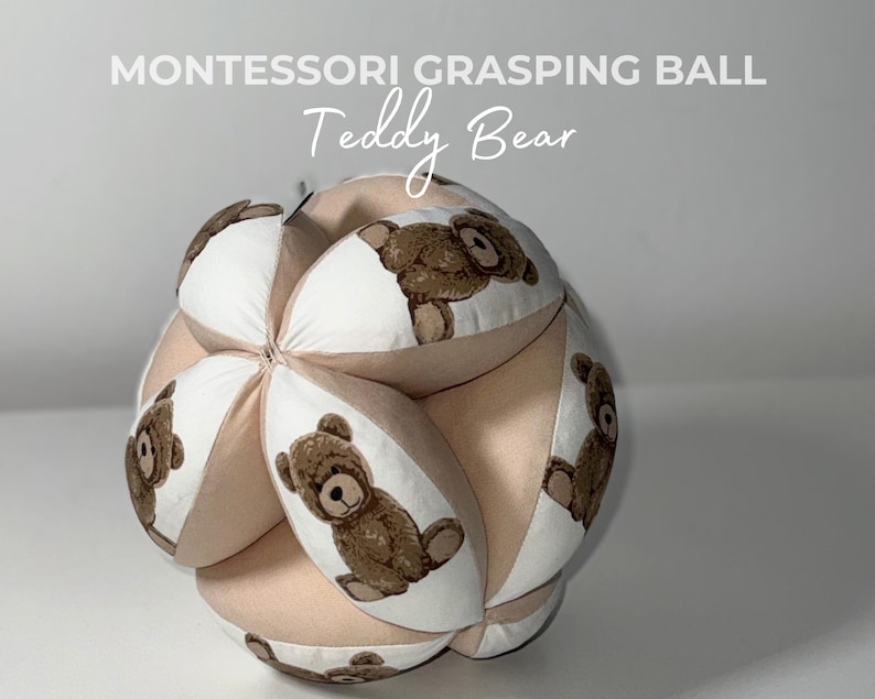 May include: A beige and white Montessori grasping ball with a teddy bear design. The ball is made of soft fabric and has six panels, each with a different teddy bear image.