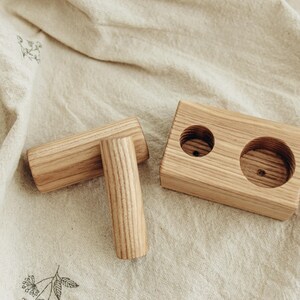 May include: Wooden candle holder set with two cylindrical candle holders and a rectangular base with two circular openings. The wood has a natural grain and light brown color. The set is designed for candles.