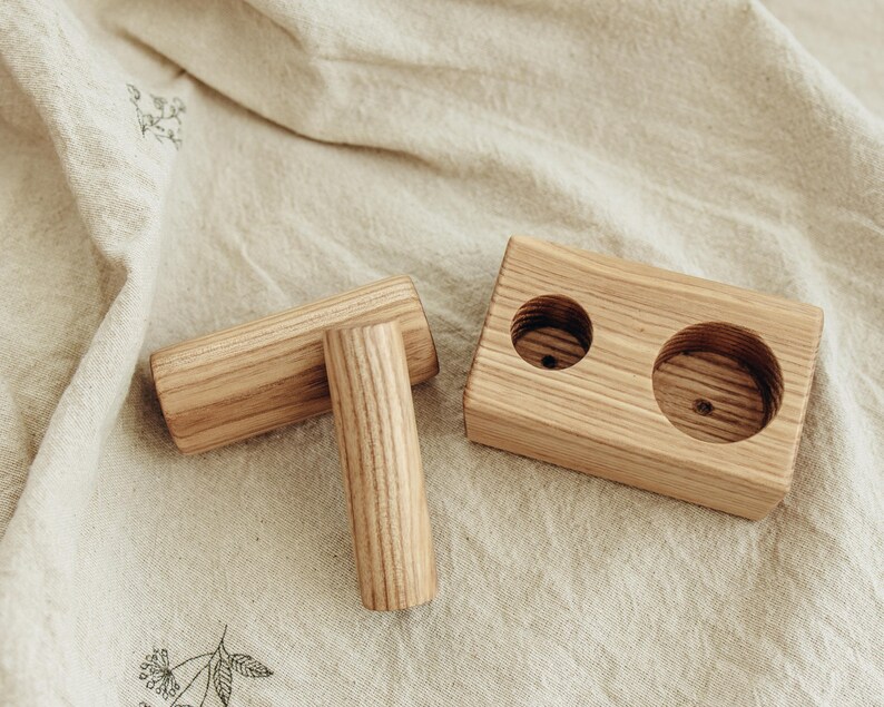 May include: Wooden candle holder set with two cylindrical candle holders and a rectangular base with two circular openings. The wood has a natural grain and light brown color. The set is designed for candles.