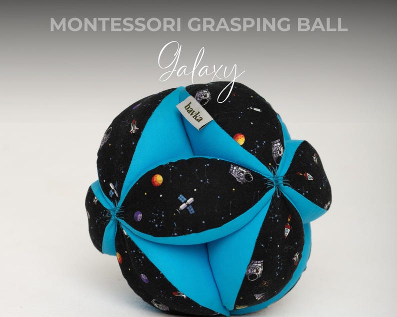 May include: A blue and black fabric grasping ball with a galaxy print. The ball has a tag that says "bawka" on it. The ball is a Montessori toy for babies and toddlers.