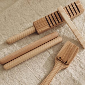 Könnte beinhalten: Ein Set aus hellbraunen Holzküchenutensilien, bestehend aus einer rechteckigen Reibe mit Griff, zwei glatten zylindrischen Nudelhölzern und einem flachen Pfannenwender mit einem kleinen Loch oben, alle mit natürlicher Holzmaserung.