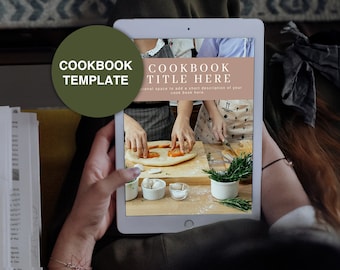 May include: A digital tablet displaying a cookbook template with the text "COOKBOOK TITLE HERE" and a photo of two people making pizza. The text below the title reads "Optional space to add a short description of your cookbook here."