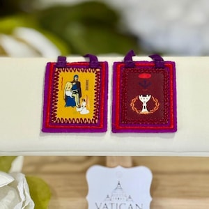 May include: Two small, rectangular religious pendants with purple trim and loops. One features a yellow background with a religious scene, the other a burgundy background with a chalice. A Vatican tag is in the foreground.