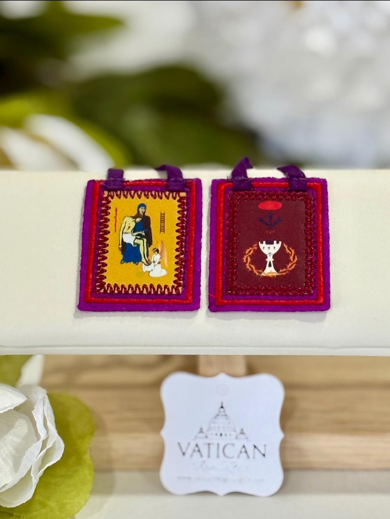 May include: Two small, rectangular religious pendants with purple trim and loops. One features a yellow background with a religious scene, the other a burgundy background with a chalice. A Vatican tag is in the foreground.