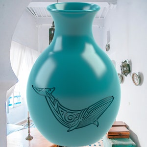 May include: A teal-colored ceramic vase with a whale design. The vase has a rounded body and a flared rim. The whale design is a stylized, tribal-inspired illustration. The vase is suspended in a room with white walls and a patterned tile floor.