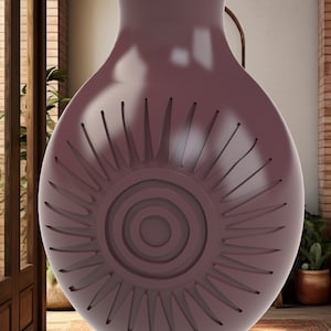 Puede incluir: Un jarrón de cerámica de color morado oscuro con un diseño de sol. El jarrón tiene una base ancha y un cuello estrecho.