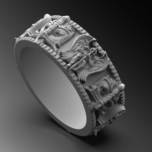 Könnte beinhalten: Ein silberner Ring mit einem detaillierten Design von drei Gesichtern, jedes mit einem anderen Ausdruck. Die Gesichter sind von komplizierten Details umgeben, darunter Flügel und Hörner.