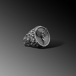 Puede incluir: Un anillo de plata con un dise&ntilde;o ovalado que presenta una imagen esculpida detallada de un &aacute;ngel con alas. La banda del anillo est&aacute; intrincadamente dise&ntilde;ada con patrones florales.