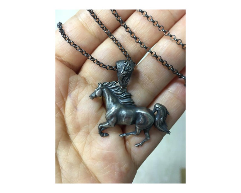 Puede incluir: Un collar de plata con un colgante de caballo con un dise&ntilde;o detallado. El caballo est&aacute; corriendo y tiene una melena y una cola fluidas. El collar est&aacute; en una cadena negra.