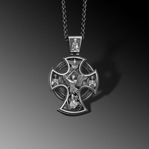 May include: A silver pendant with a cross design featuring an angel with wings and a sword. The cross has four smaller images of saints and the words "СВЯТЫЙ ХРИСТОС" and "ИСТА АНГЕЛ" around the perimeter.