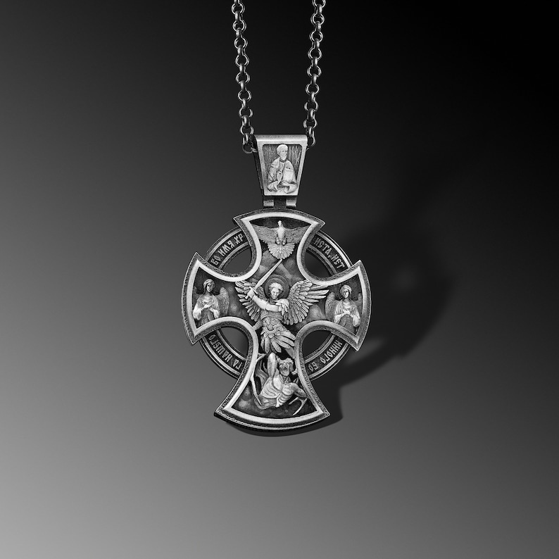 May include: A silver pendant with a cross design featuring an angel with wings and a sword. The cross has four smaller images of saints and the words "СВЯТЫЙ ХРИСТОС" and "ИСТА АНГЕЛ" around the perimeter.