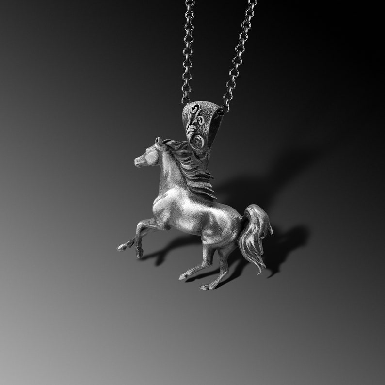 Puede incluir: Un collar con un colgante de plata en forma de caballo. El caballo est&aacute; en posici&oacute;n de alzada, con la cabeza girada hacia un lado. El colgante est&aacute; unido a una cadena de plata.